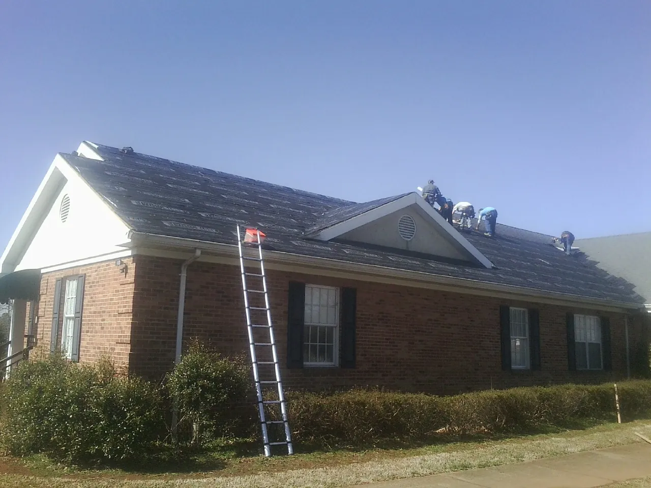 Crew tearing shingles off a brick ranch roof with a ladder set — Emergency Roof Repair work by our crew in Ironton