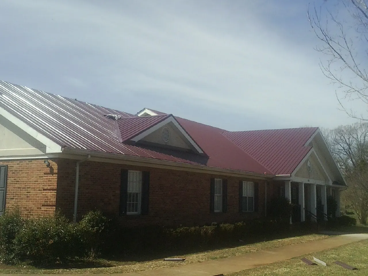 Red metal roof with gabled entries on a long brick building, from a Hail Damage Roof Repair job in Ironton
