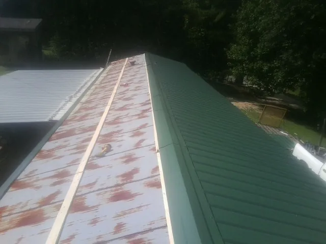 Old rusted panels beside newly installed green metal roofing — Wind Damage Roof Repair by Roofing Brothers in Ironton