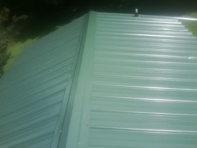 New green metal panels meeting at the ridge of a roof — Flat Roof Repair work by our crew in Ironton