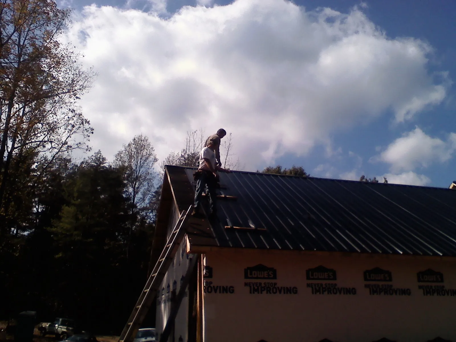 Roofer fastening dark metal panels high against a cloudy sky, from a Roof Inspection job in Ironton