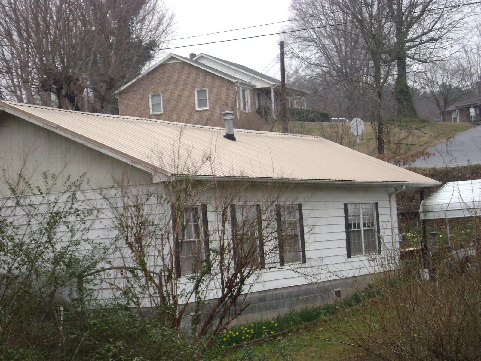 Tan metal roof on a white sided house set into a hillside — Commercial Roofing by Roofing Brothers in Ironton